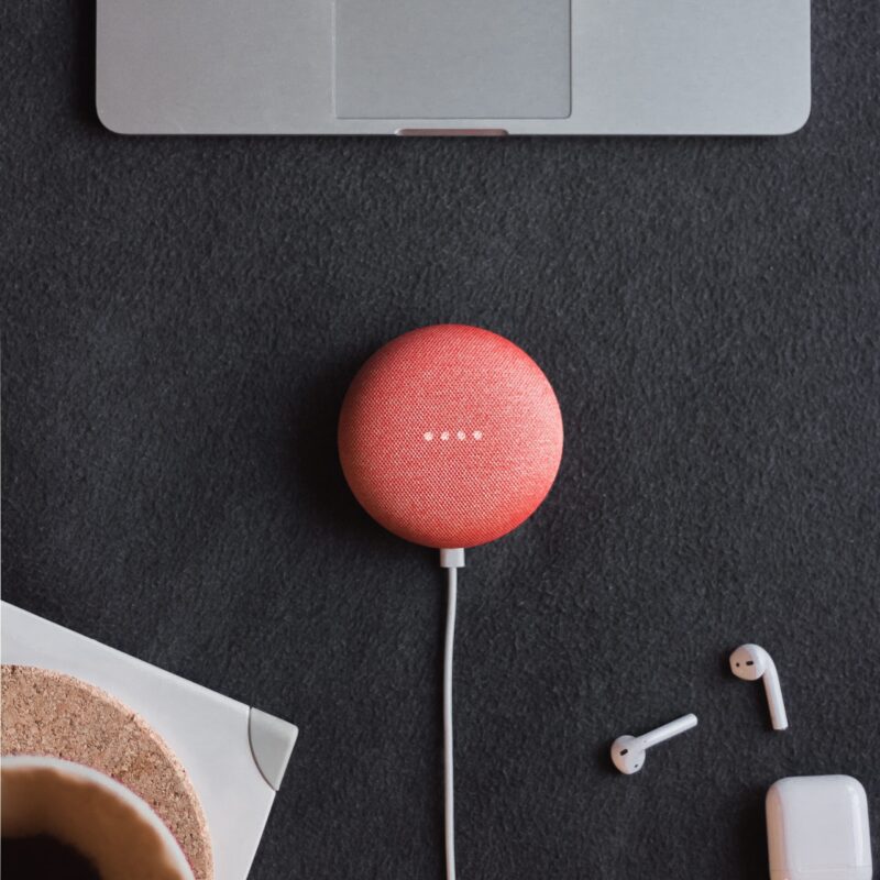 flat lay photography of coral Google Home Mini on black surface beside Apple AirPods